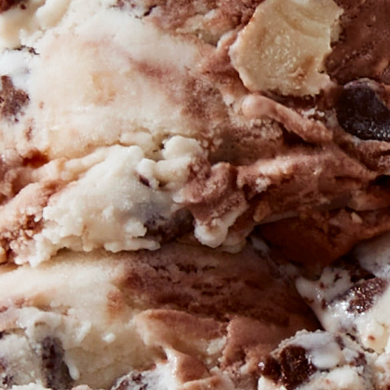 Extreme close-up texture shot of N!CK'S Brownie Cookie Dough light ice cream, showing swirls of vanilla and chocolate ice cream with visible chunks of brownie and cookie dough pieces.
